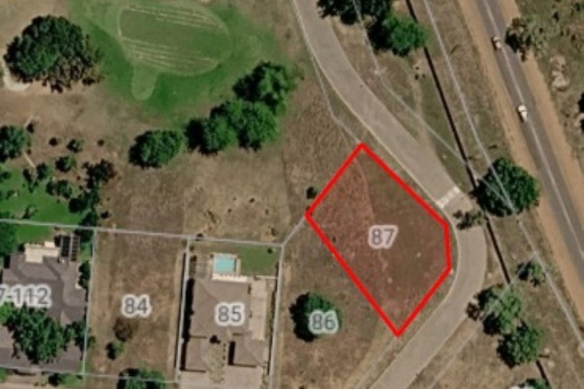 Aerial view of vacant residential plot number 87, situated in a developed estate with surrounding infrastructure and road access.