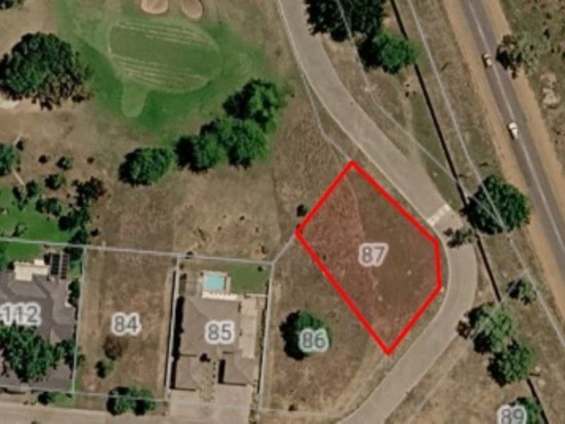 Aerial view of vacant residential plot number 87, situated in a developed estate with surrounding infrastructure and road access.