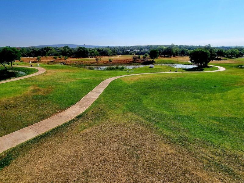 A scenic elevated view of a well-maintained golf course featuring lush green fairways, water hazards, and paved walking paths.