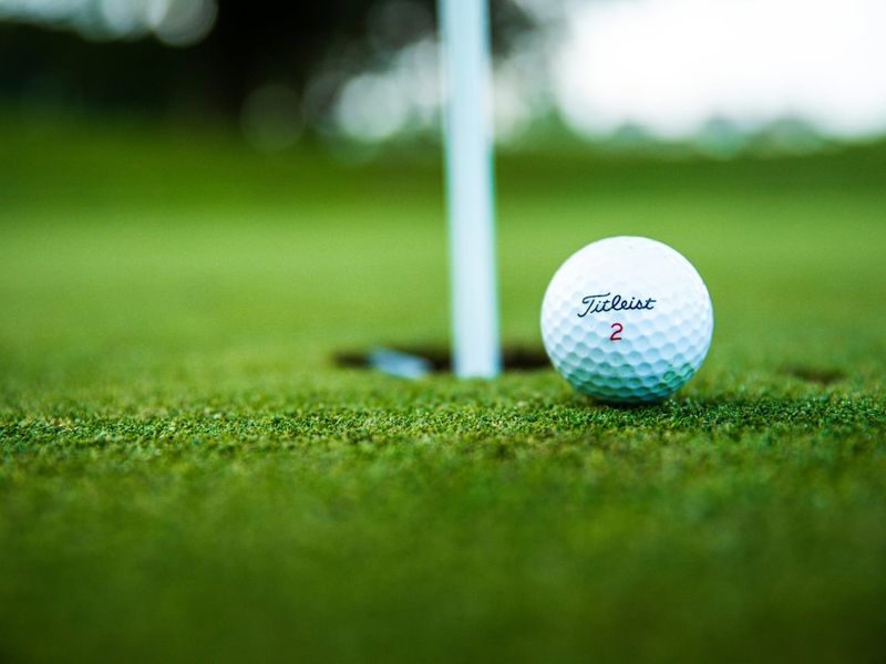 A close-up view of a golf ball on a well-maintained putting green with a flagstick.