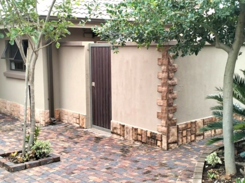 Front entrance area featuring a paved driveway, stone-clad wall accents, a timber front door, and established garden landscaping.