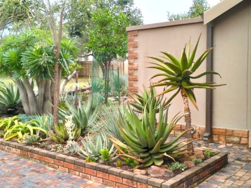 A well-maintained garden area featuring a raised brick planter bed, stone-clad wall accents, and established succulent landscaping alongside a paved driveway.