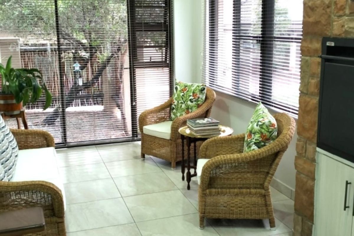 A bright sunroom or living area featuring tiled floors, a stone-clad fireplace, and large sliding glass doors with venetian blinds overlooking the garden.