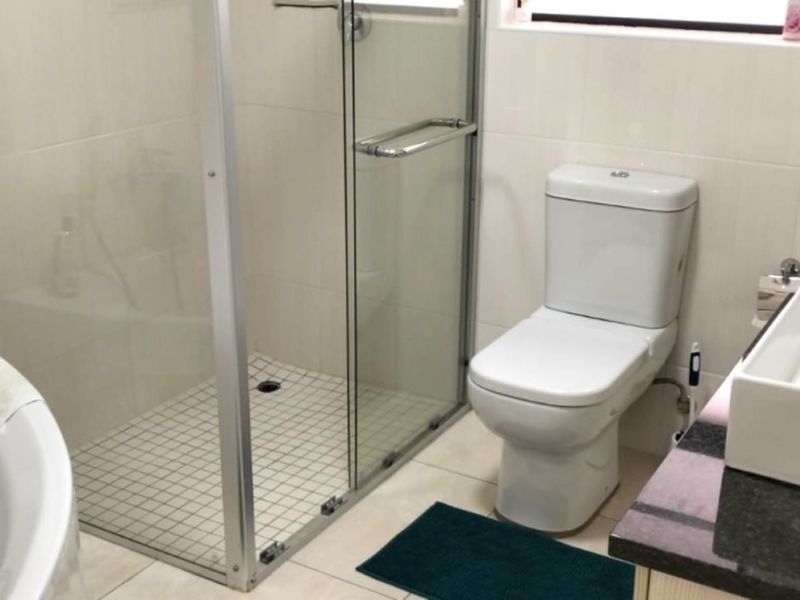 A functional bathroom featuring a glass shower enclosure, a freestanding bathtub, a modern vessel sink, and neutral wall and floor tiling.
