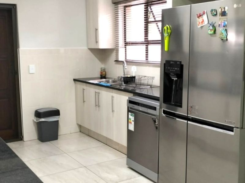 A functional kitchen featuring light-toned cabinetry, dark granite countertops, tiled flooring, and a tiled backsplash with integrated dishwasher and gas hob.
