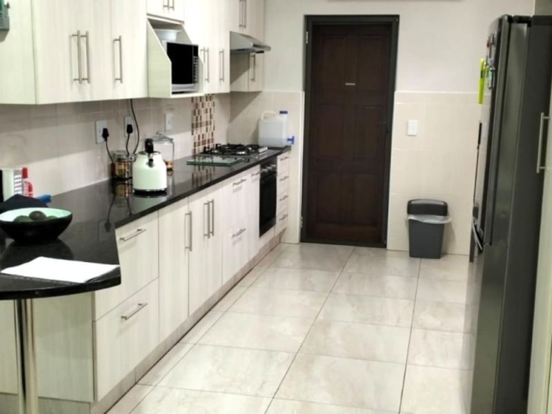 A functional kitchen featuring light-toned cabinetry, dark granite countertops, a gas hob, built-in oven, and neutral tiled flooring.