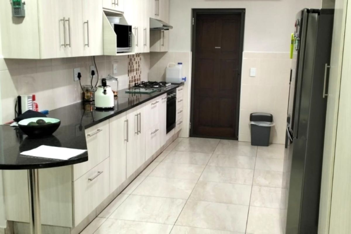 A functional kitchen featuring light-toned cabinetry, dark granite countertops, a gas hob, built-in oven, and neutral tiled flooring.