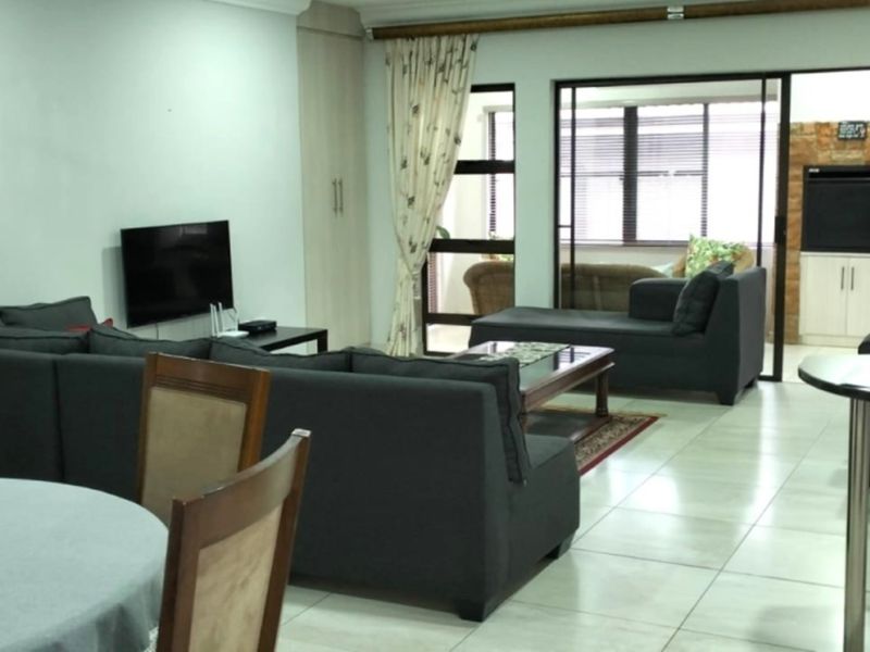Spacious open-plan living area featuring tiled flooring, a stone feature wall, and sliding glass doors leading to an adjoining space.