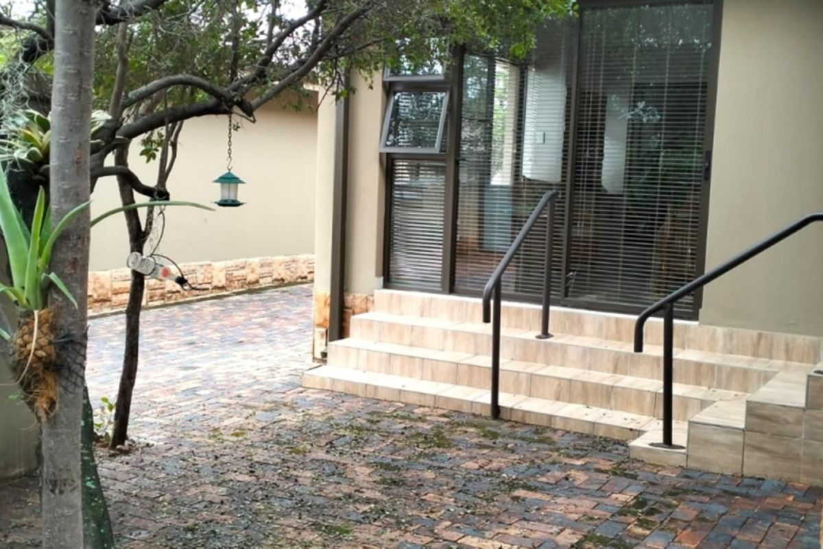 Rear exterior view featuring a brick paved patio area with tiled steps, metal handrails, and sliding glass door access to the home.