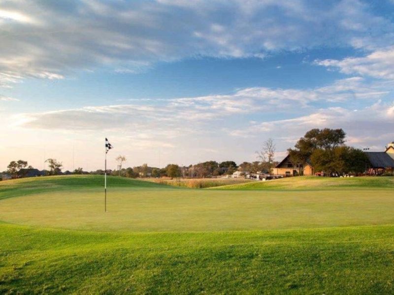 A scenic view of a well-maintained golf course putting green with a flagstick, featuring a clubhouse in the background.