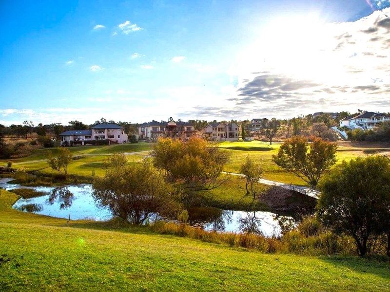 A scenic view of the residential estate grounds featuring manicured lawns, a natural water feature, and a pedestrian bridge.