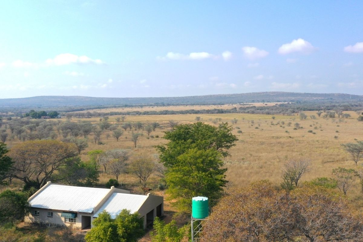 Aerial view of the farm property featuring a building with a metal roof and an elevated water storage tank set against a vast landscape.