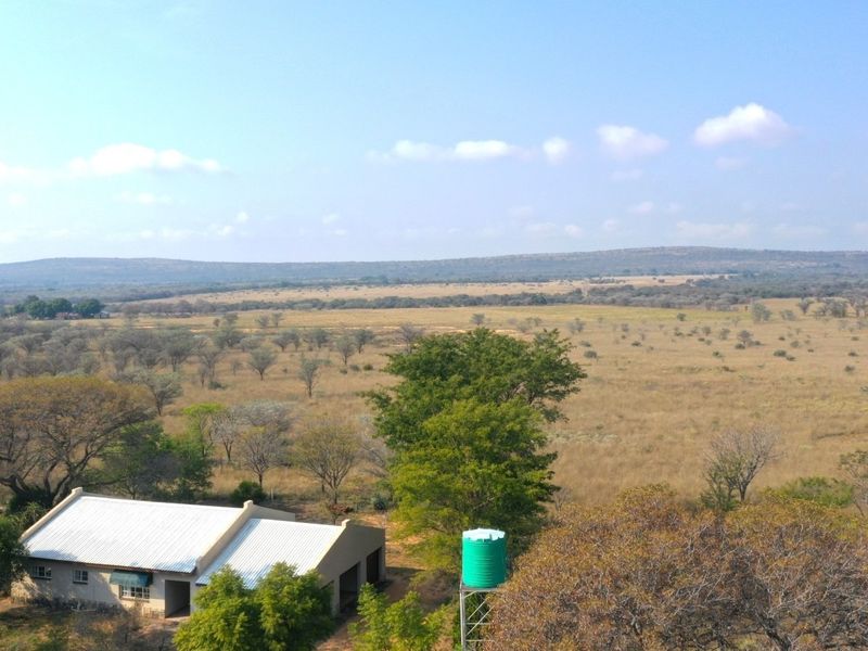 Aerial view of the farm property featuring a building with a metal roof and an elevated water storage tank set against a vast landscape.