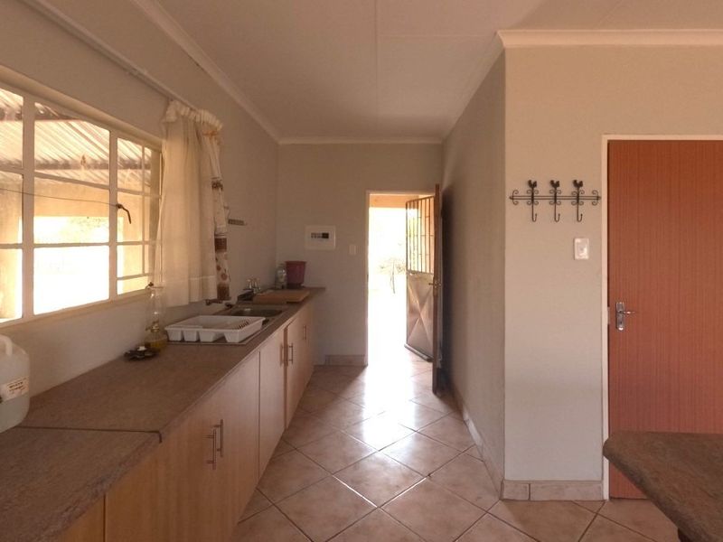 A functional kitchen area featuring built-in cabinetry, laminate countertops, a stainless steel sink, and tiled flooring with direct access to the exterior.