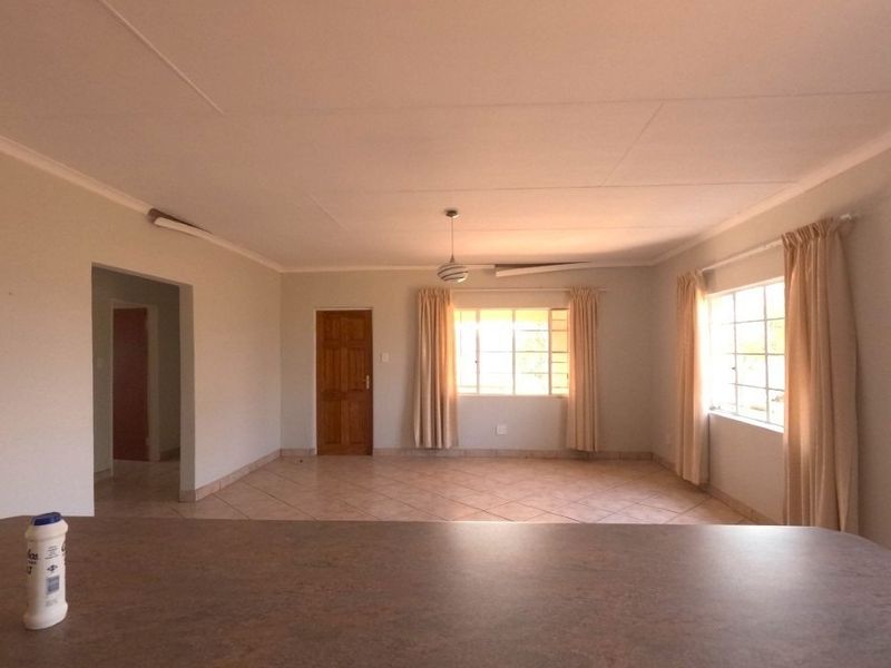 Spacious, light-filled living area featuring neutral tiled flooring, coved ceilings, and large windows, offering a versatile blank canvas for interior design.