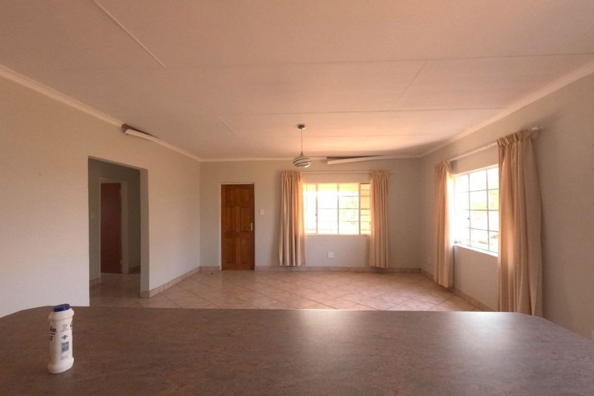 Spacious, light-filled living area featuring neutral tiled flooring, coved ceilings, and large windows, offering a versatile blank canvas for interior design.