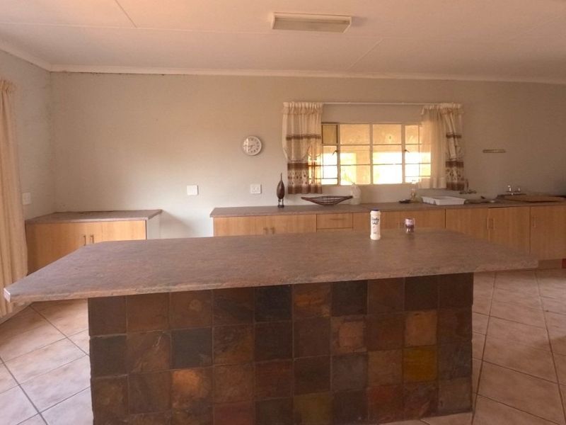 A spacious kitchen featuring a central island with a tiled base, laminate countertops, built-in cabinetry, and a double sink with ceramic floor tiles.