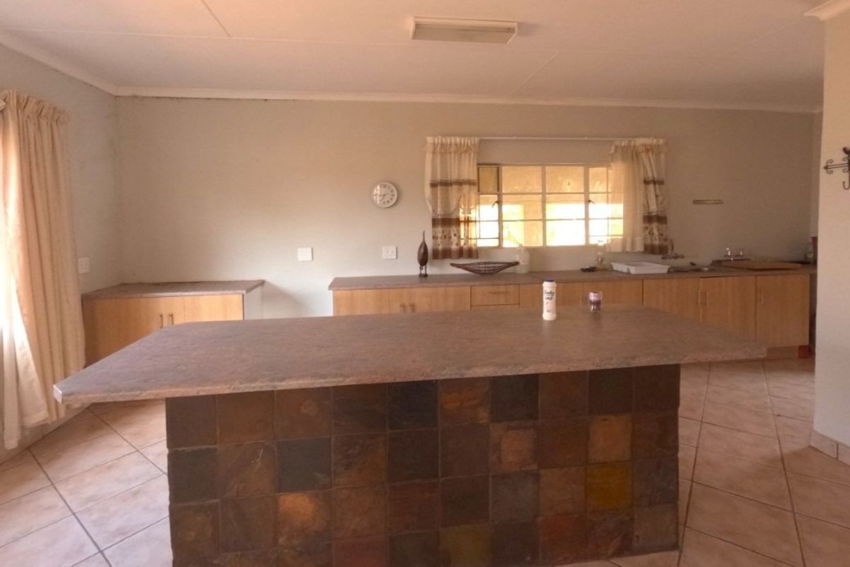 A spacious kitchen featuring a central island with a tiled base, laminate countertops, built-in cabinetry, and a double sink with ceramic floor tiles.