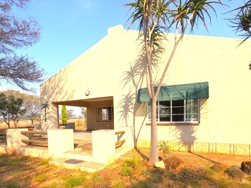 Rear view of the farm dwelling featuring a covered patio area, timber railings, and steel-framed windows set within a natural landscape.
