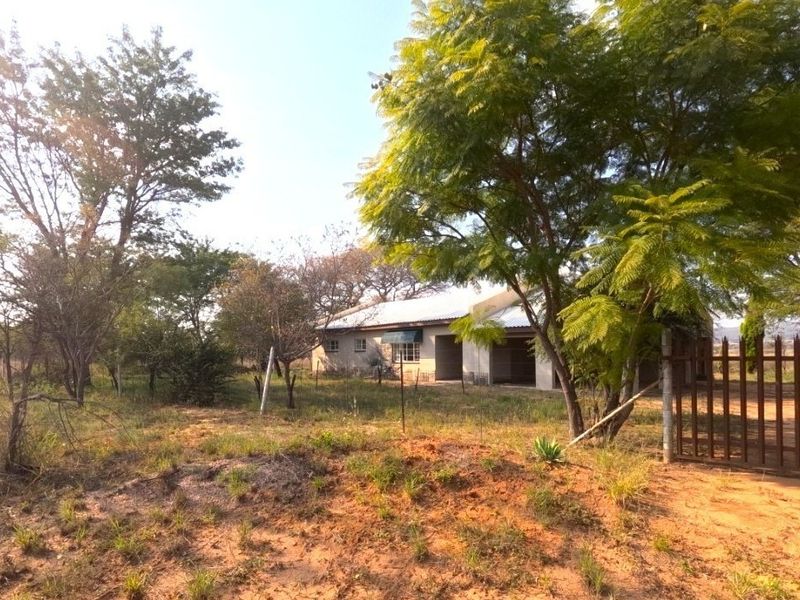 A view of the farm property entrance featuring a metal gate, perimeter fencing, and a single-story dwelling with a corrugated metal roof.