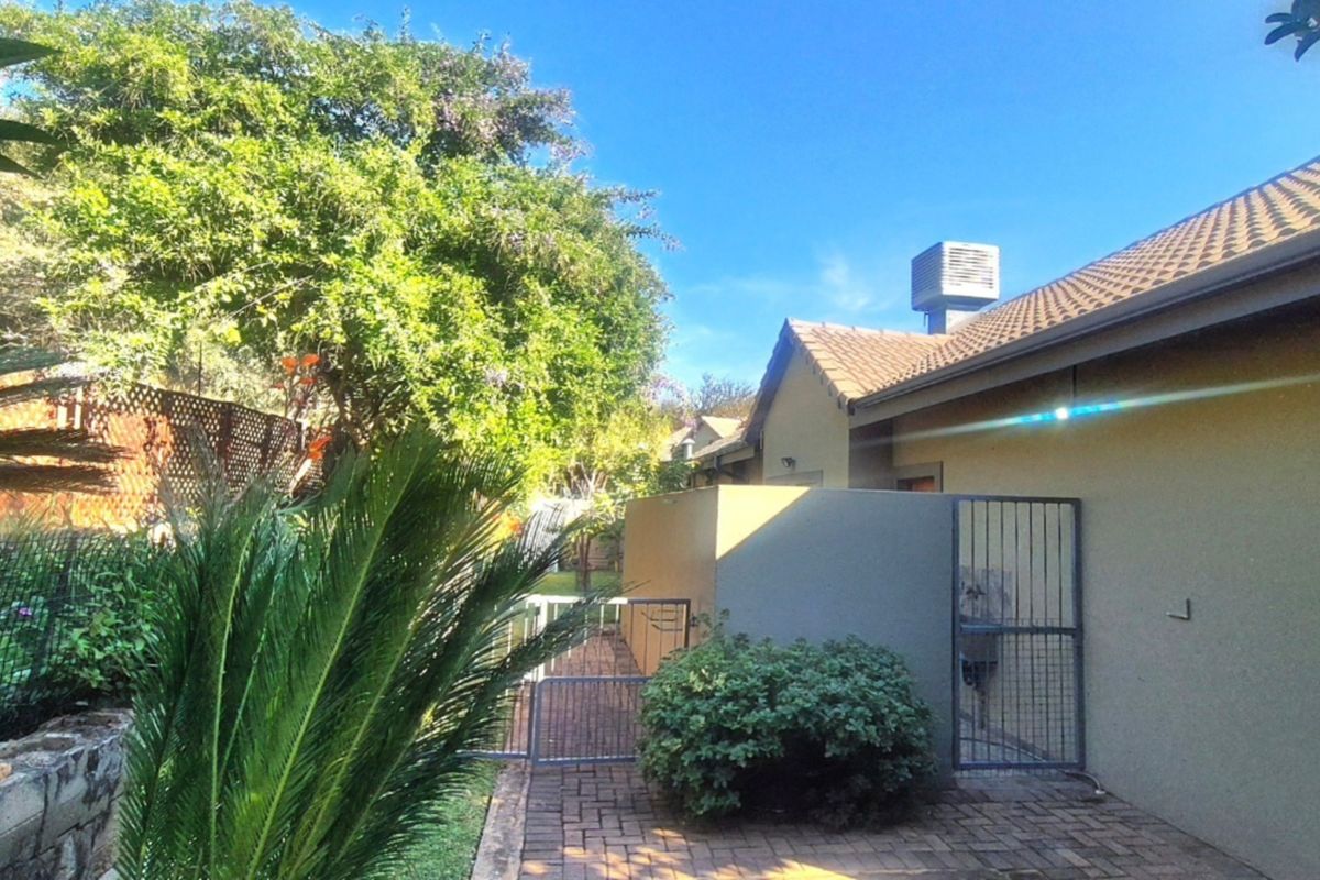 A view of the rear exterior featuring a paved walkway, metal security gate, and established garden area with a tiled roof structure.