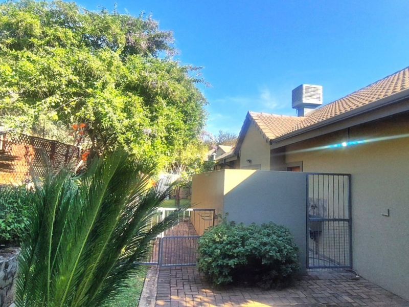 A view of the rear exterior featuring a paved walkway, metal security gate, and established garden area with a tiled roof structure.
