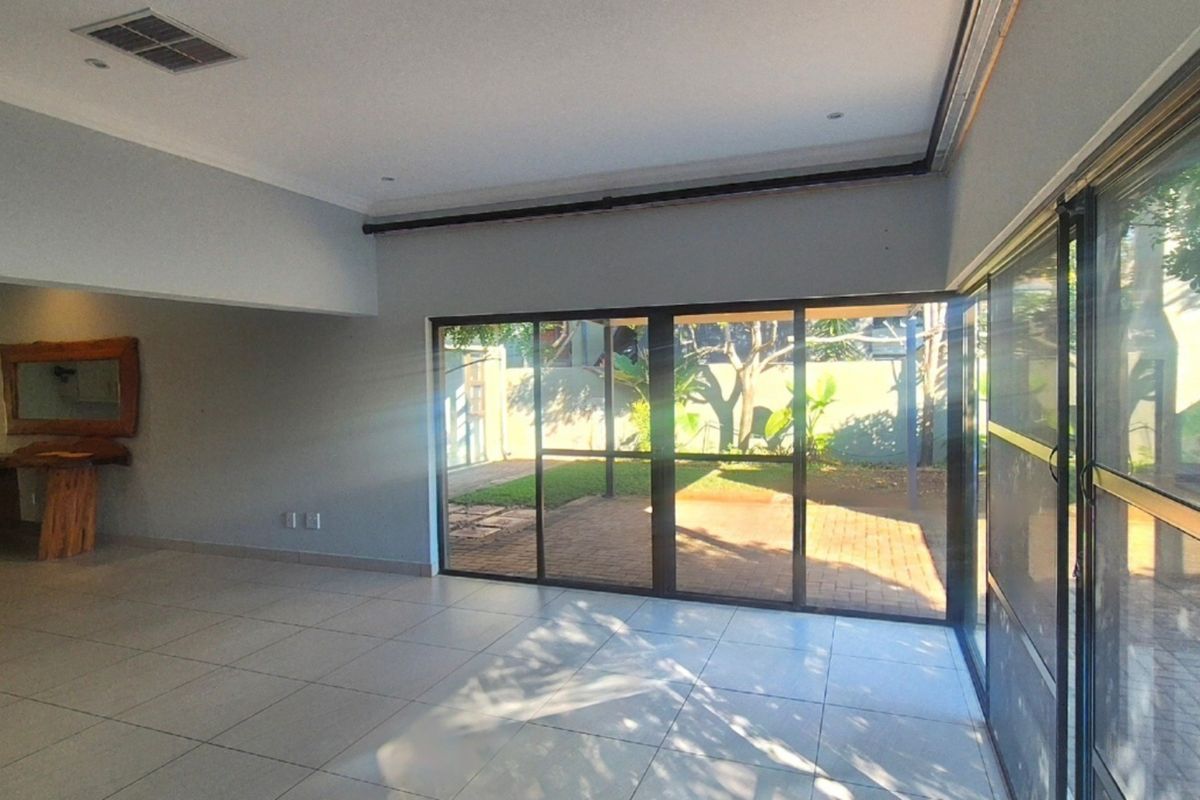 Spacious living area featuring large sliding glass doors that open to a paved patio and garden, with neutral tiled flooring and recessed lighting.