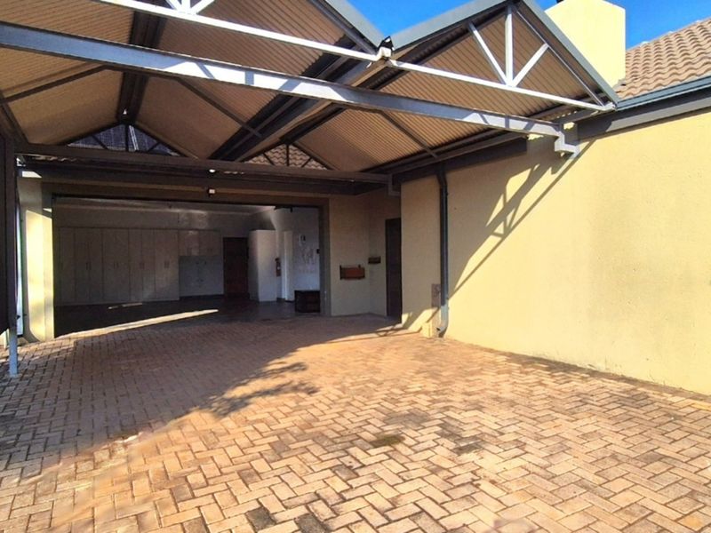 Spacious covered carport area featuring paved flooring and integrated built-in storage cupboards, providing ample space for vehicle parking and additional utility storage.