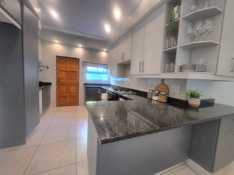 Modern kitchen featuring dark grey cabinetry, granite countertops, a gas hob, and tiled flooring with ample storage and open shelving.