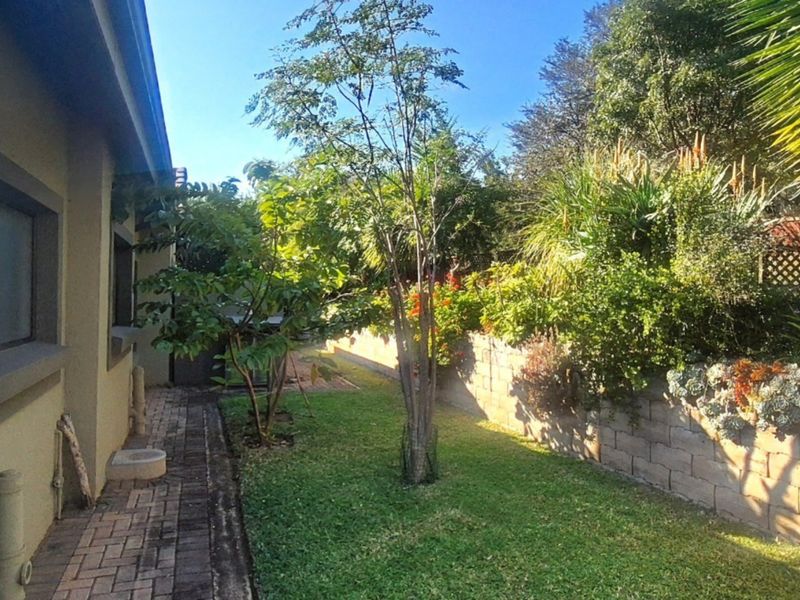 A well-maintained rear garden featuring a brick-paved walkway, established trees, and a stone retaining wall.