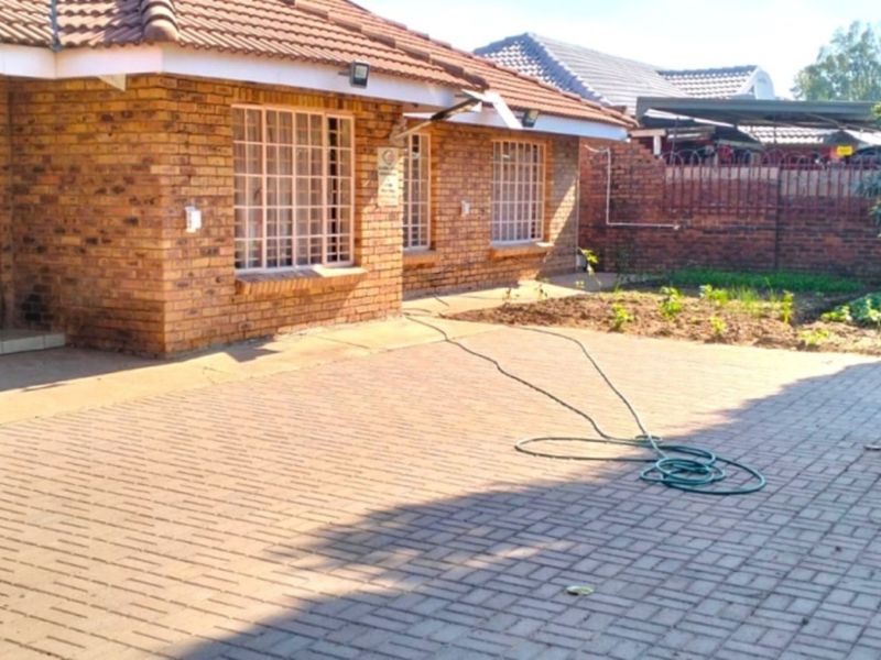 A rear exterior view of a face brick house featuring a paved patio area and a brick boundary wall.