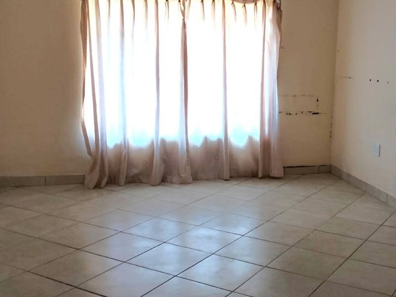 An empty living room featuring tiled flooring and neutral walls, requiring cosmetic updates and paintwork to restore its appeal.