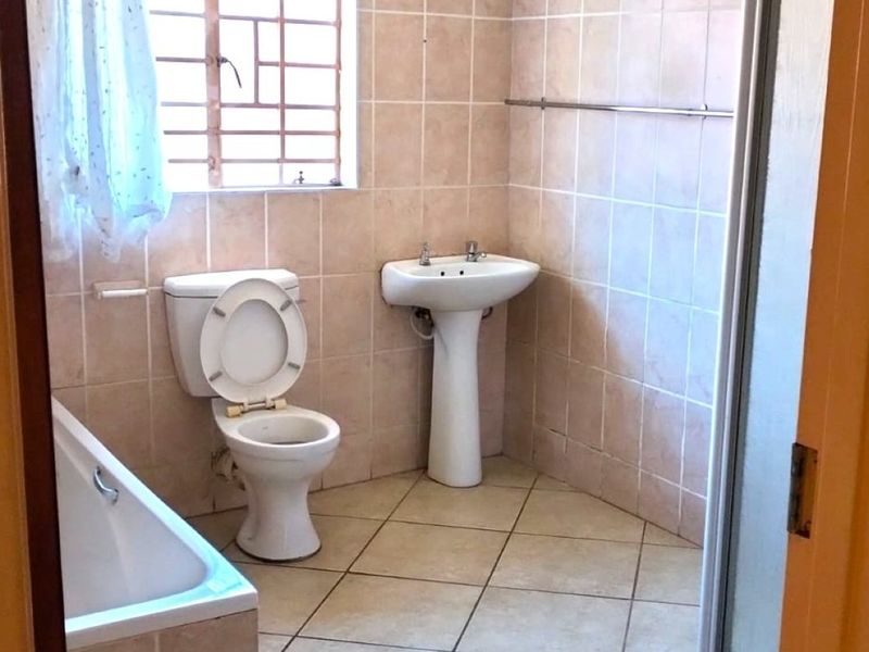 A functional bathroom featuring a pedestal basin, toilet, and bathtub with tiled finishes and security bars on the window.