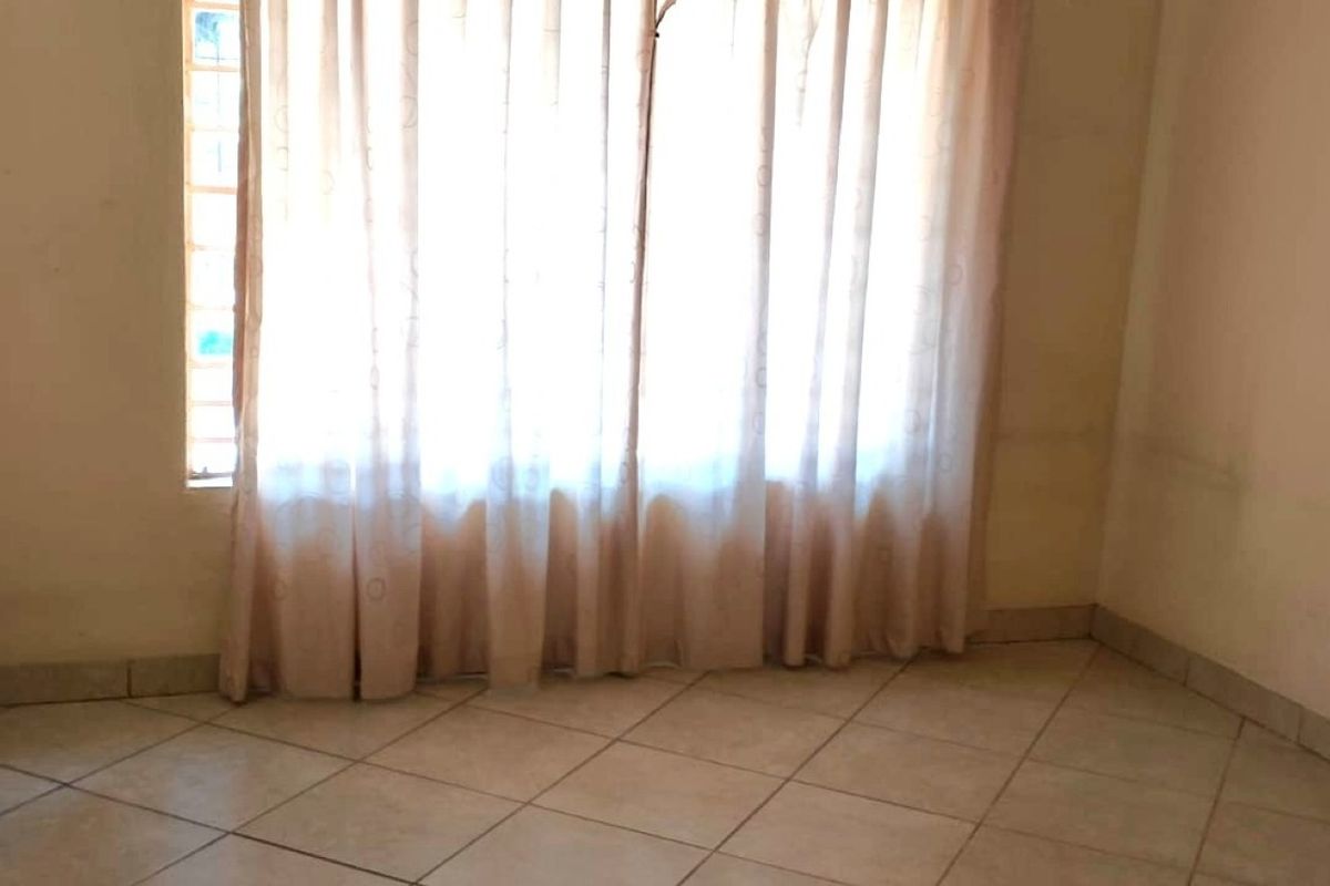 An empty bedroom featuring tiled flooring and a window with curtains, showing signs of wear on the walls.