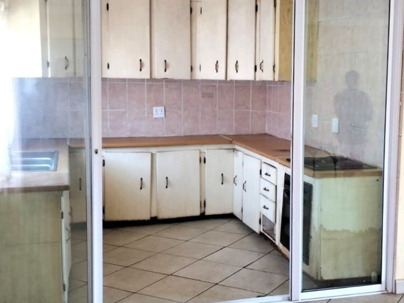 A dated kitchen featuring original cabinetry, laminate countertops, and tiled flooring, viewed through a sliding glass door. Ideal for a modern renovation.