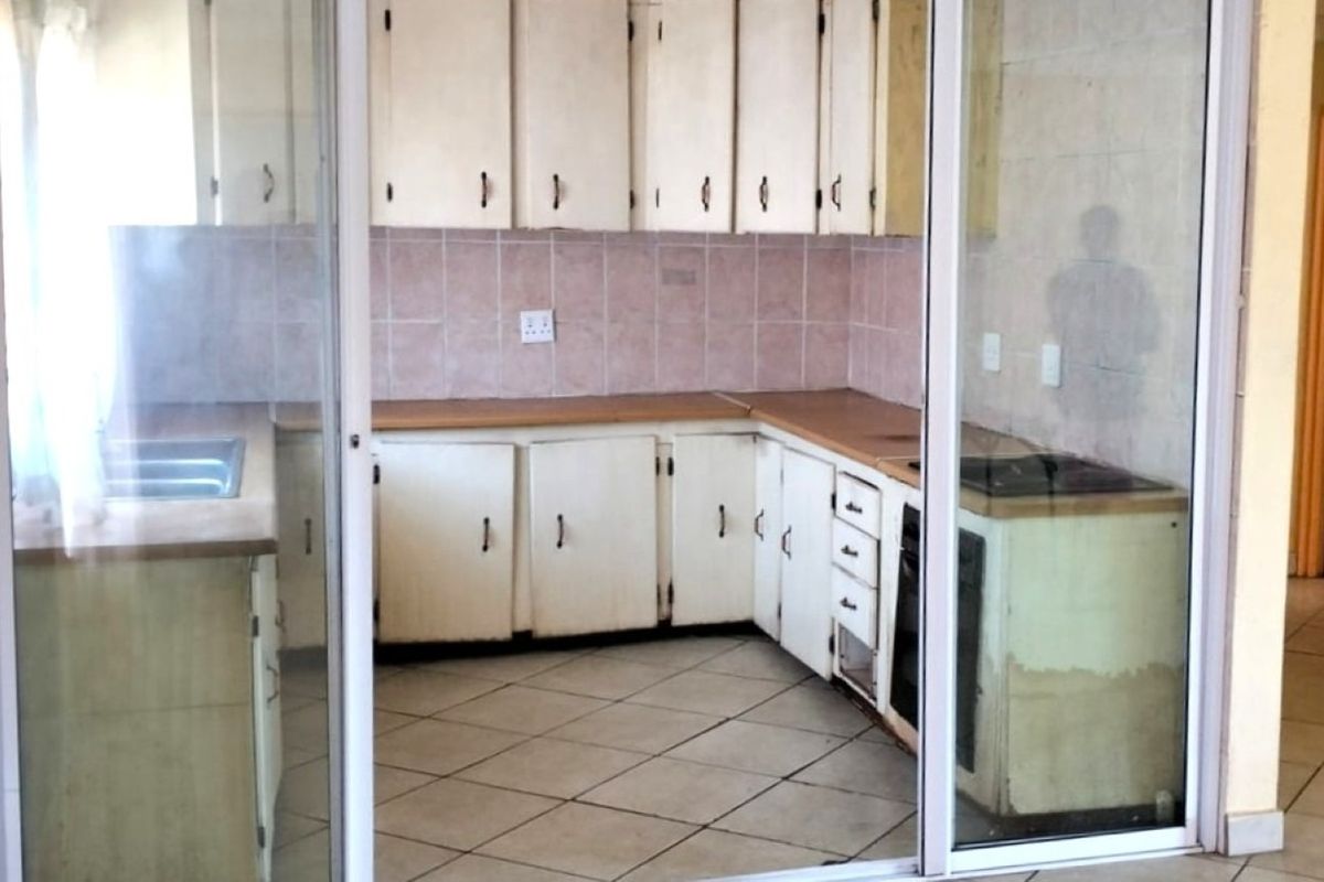 A dated kitchen featuring original cabinetry, laminate countertops, and tiled flooring, viewed through a sliding glass door. Ideal for a modern renovation.