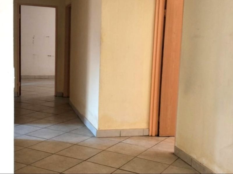 A vacant hallway featuring tiled flooring and multiple internal doorways, showing signs of wear on the wall surfaces.