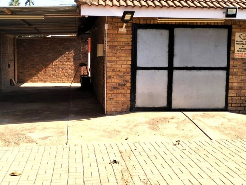 A functional garage area featuring brick construction, a tiled roof, and paved driveway access, equipped with security lighting and signage.