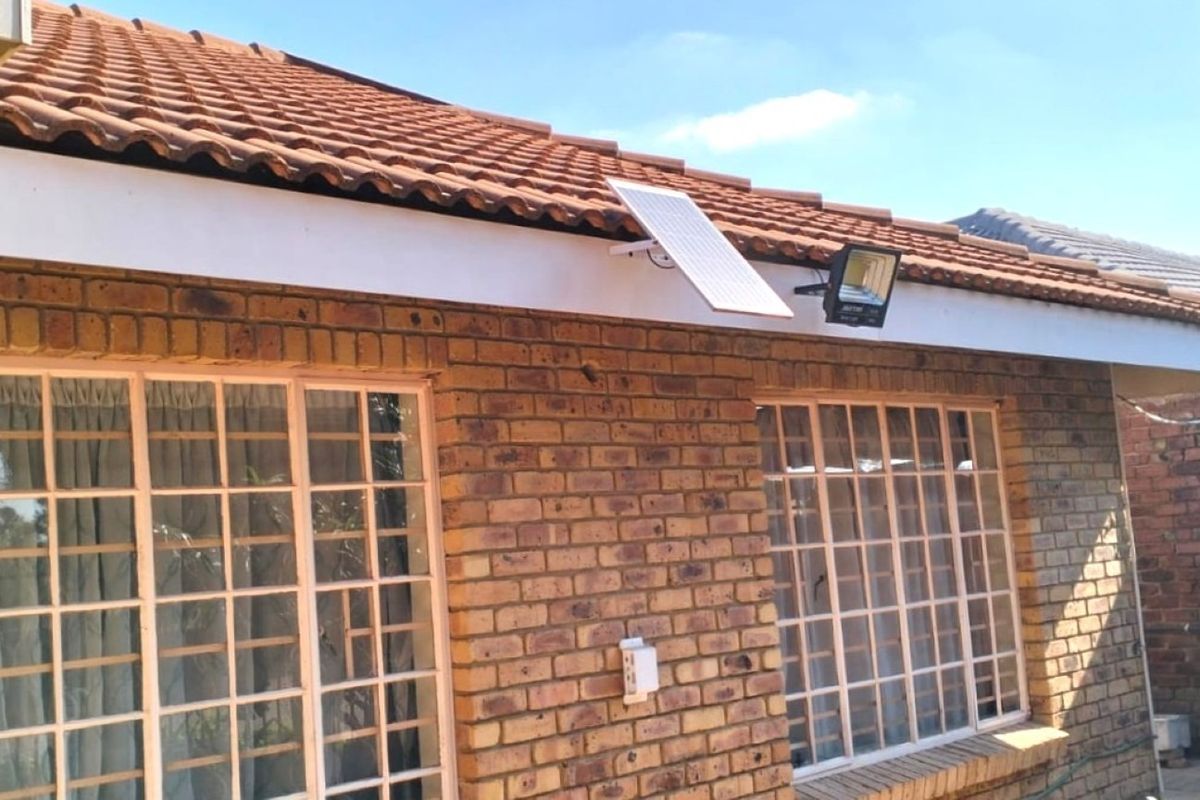 A view of the rear exterior featuring facebrick walls, terracotta roof tiles, and security-barred windows with an installed solar floodlight.