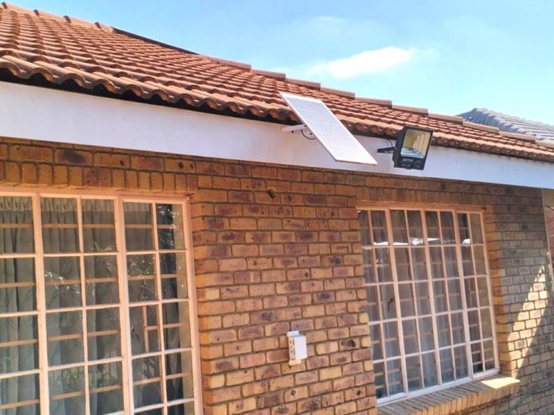 A view of the rear exterior featuring facebrick walls, terracotta roof tiles, and security-barred windows with an installed solar floodlight.