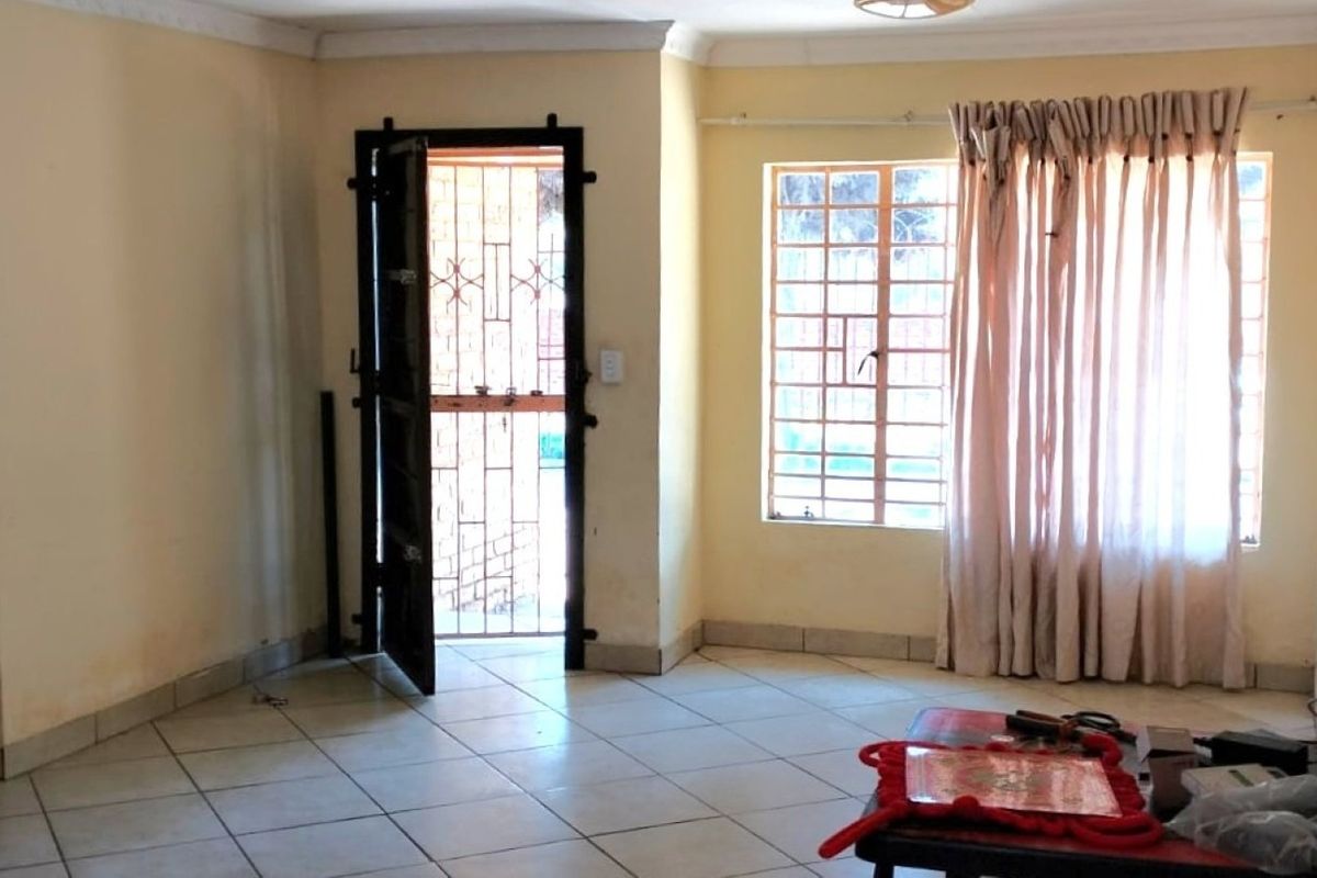 A vacant living room featuring tiled flooring, security gate, and burglar bars on the windows, requiring cosmetic updates to improve its overall appeal.