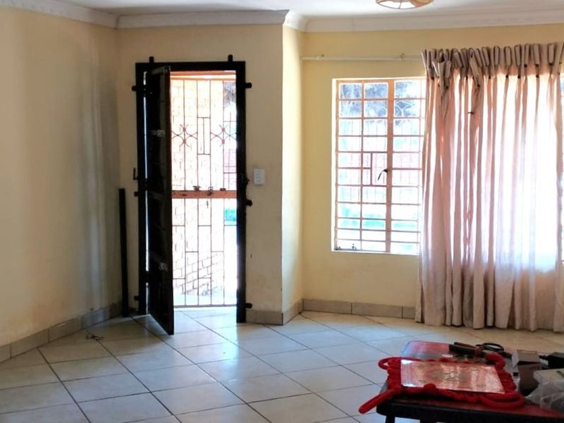 A vacant living room featuring tiled flooring, security gate, and burglar bars on the windows, requiring cosmetic updates to improve its overall appeal.