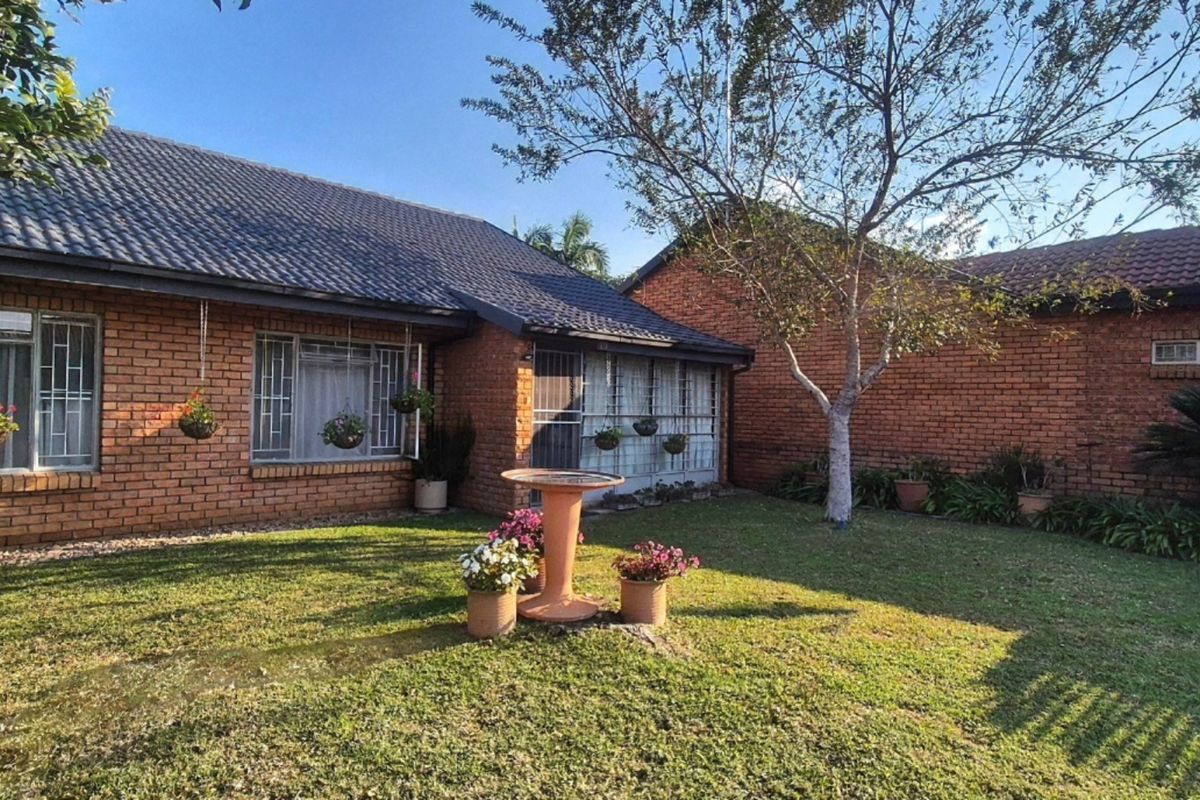 A well-maintained rear garden featuring a brick exterior, tiled roof, and established lawn with mature landscaping.