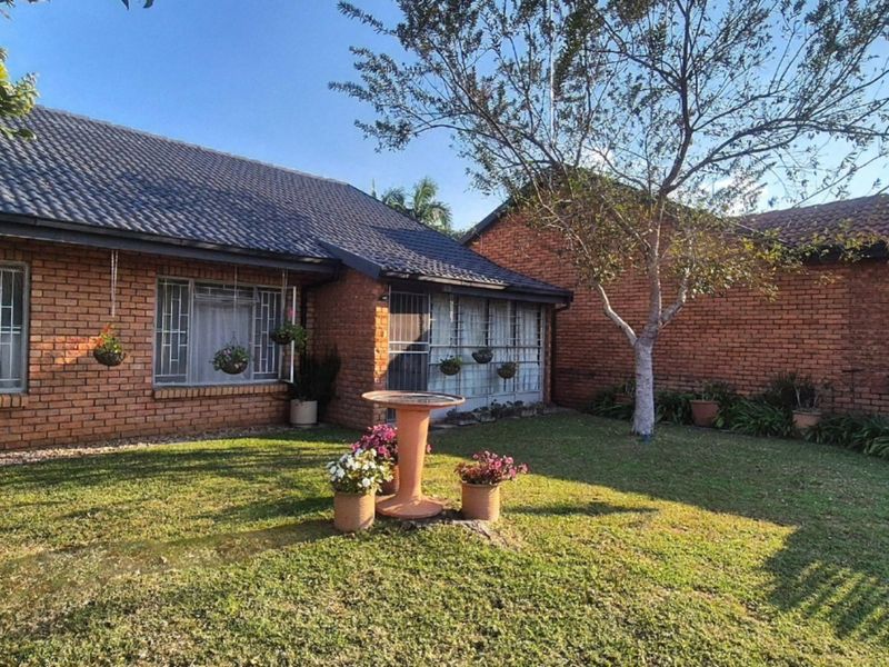A well-maintained rear garden featuring a brick exterior, tiled roof, and established lawn with mature landscaping.