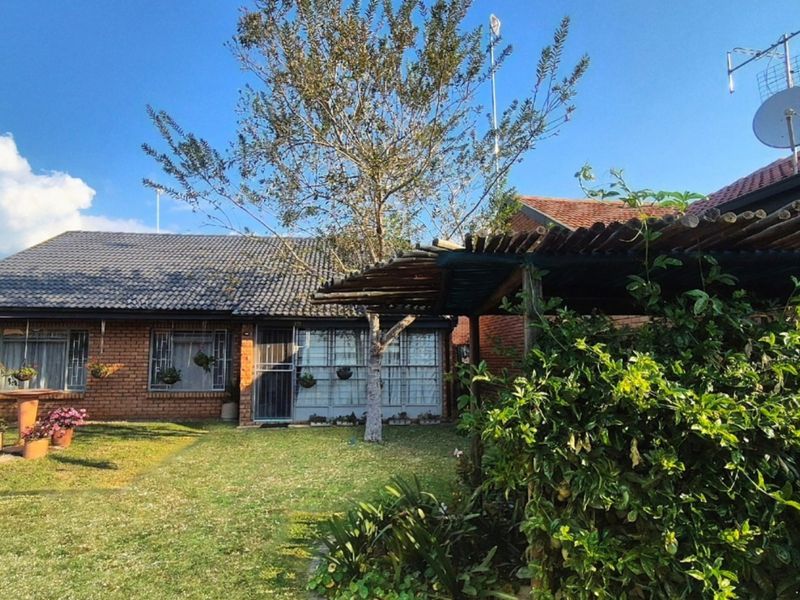 Rear view of a brick house featuring a tiled roof, a water tank, and a wooden pergola structure set within a garden area.