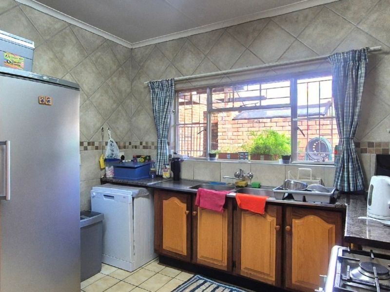 A functional kitchen featuring wooden cabinetry, laminate countertops, a stainless steel sink, and tiled wall finishes with a window overlooking the exterior.