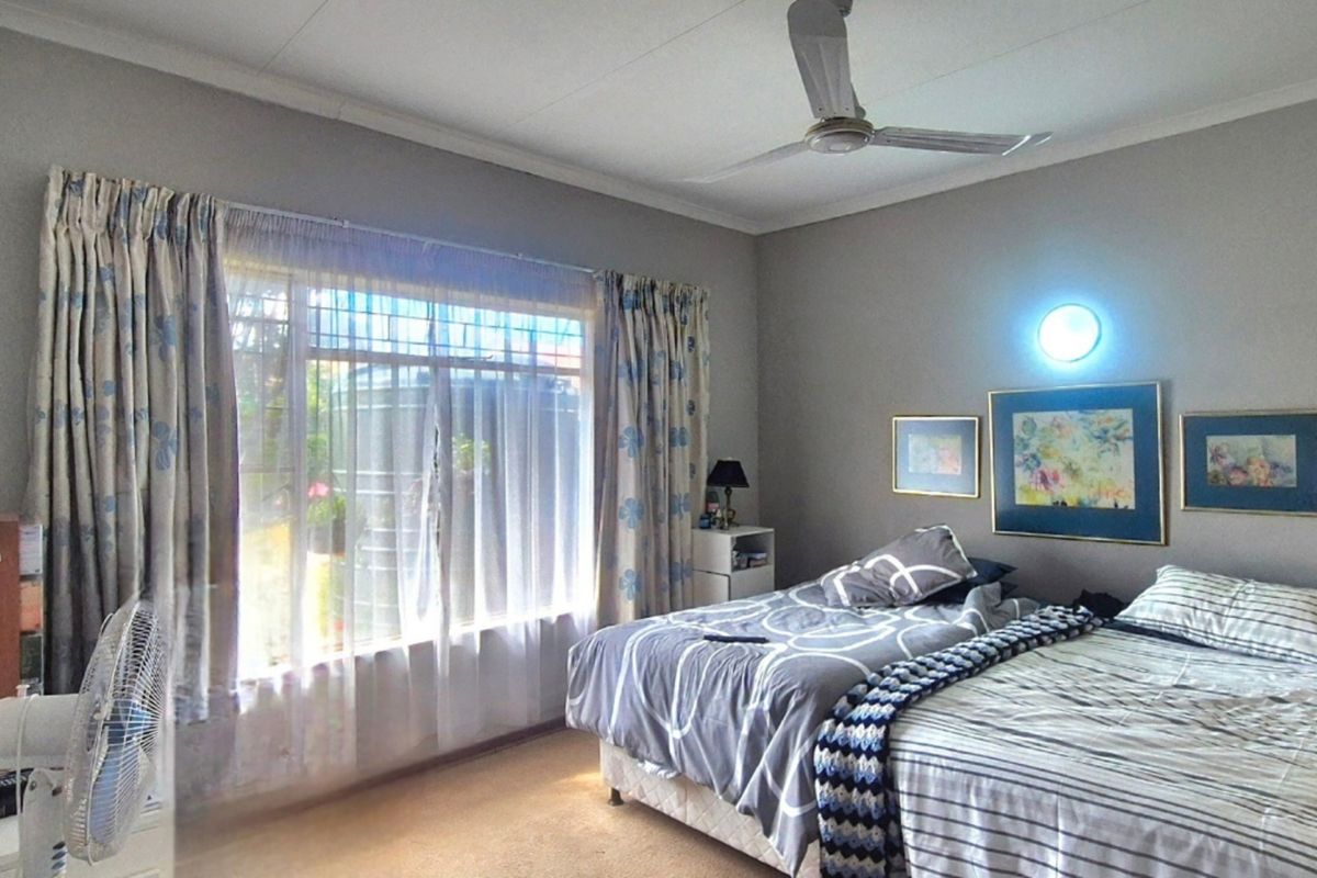 A functional bedroom featuring a ceiling fan, wall-mounted lighting, and large windows with security bars, providing natural light and ventilation.