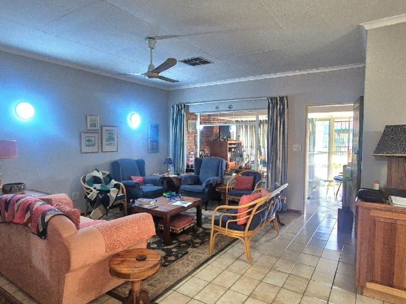 A spacious living room featuring tiled flooring, a ceiling fan, and wall-mounted lighting, with direct access to an adjoining room through a sliding glass door.