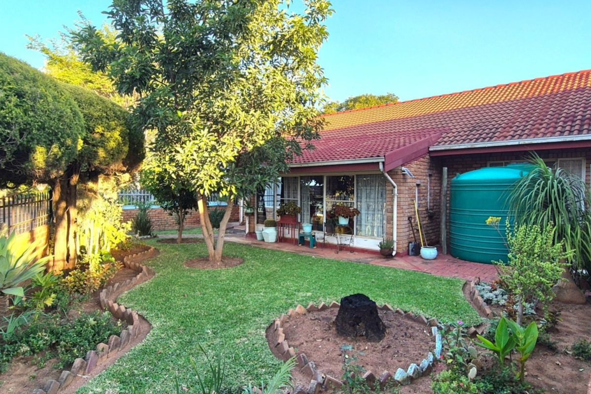 A rear view of the house featuring a brick exterior, tiled roof, paved patio area, and a well-maintained garden with a water storage tank.