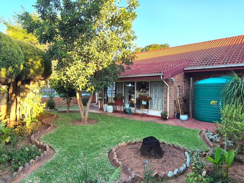 A rear view of the house featuring a brick exterior, tiled roof, paved patio area, and a well-maintained garden with a water storage tank.